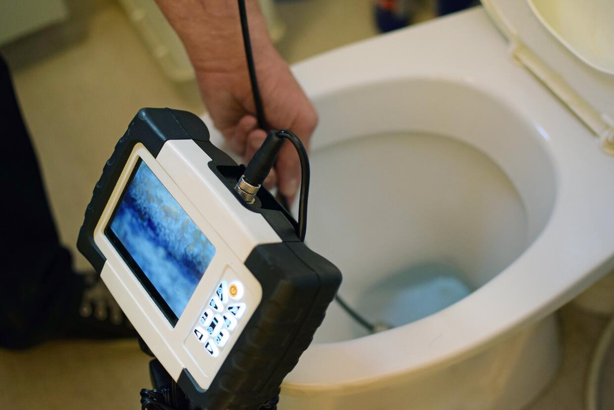 Plumber checking clogged toilet pipe with inspection camera.