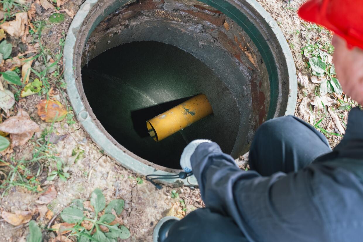 A worker with a flashlight inspects an open sewer manhole. Septic tank maintenance, sewage pumping.